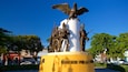 A statue of soldiers with an eagle on a pedestal, surrounded by trees and buildings.