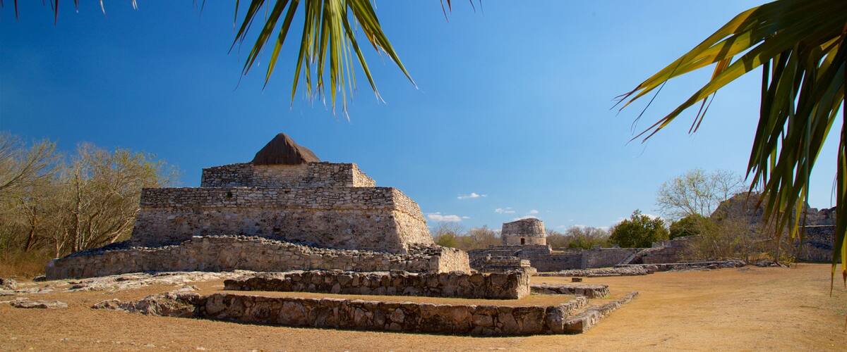 Ancient stone ruins with a pyramid-like structure surrounded by dry grass and sparse trees.