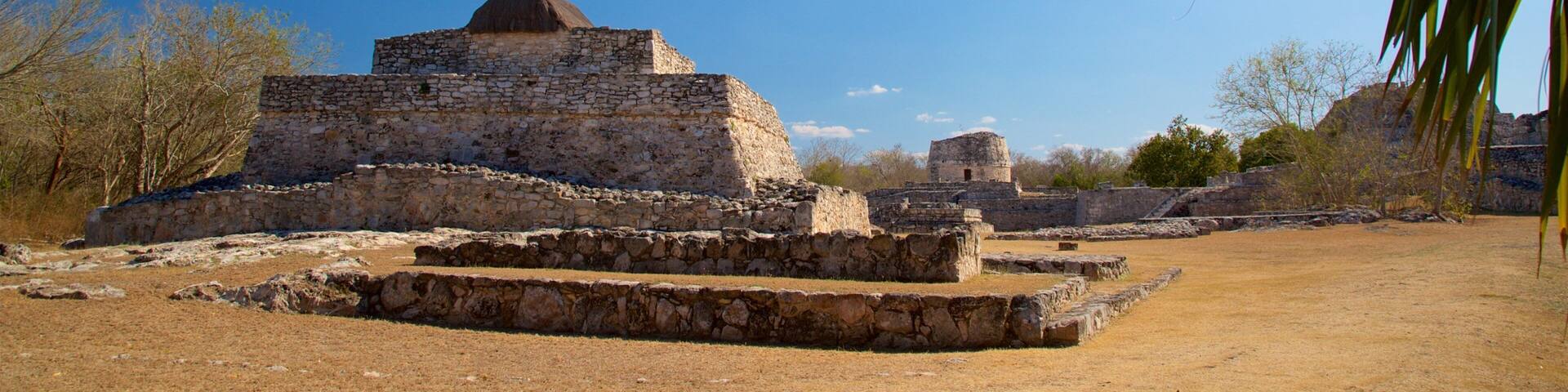Ancient stone ruins with a pyramid-like structure surrounded by dry grass and sparse trees.