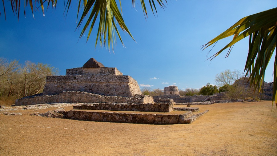 Ruinas de piedra antiguas con una estructura similar a una pirámide, rodeadas de hierba seca y árboles dispersos.