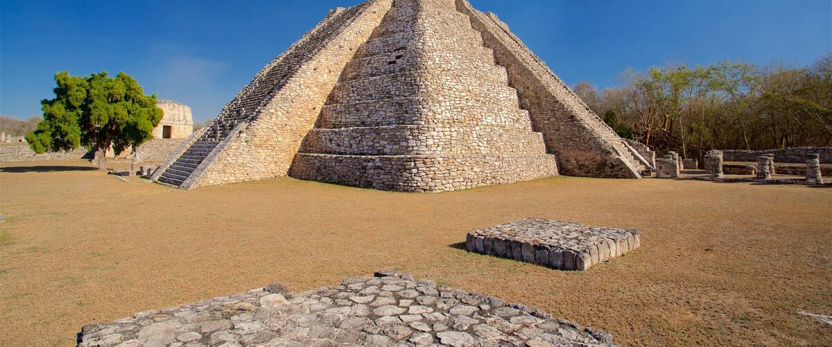 A large stone pyramid with a staircase leading to the top, surrounded by a grassy area and trees.