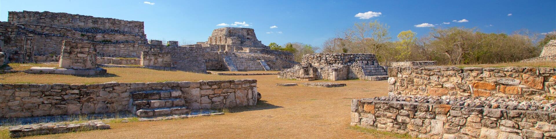 Ancient stone ruins with stepped pyramids and flat-topped structures under a clear blue sky.