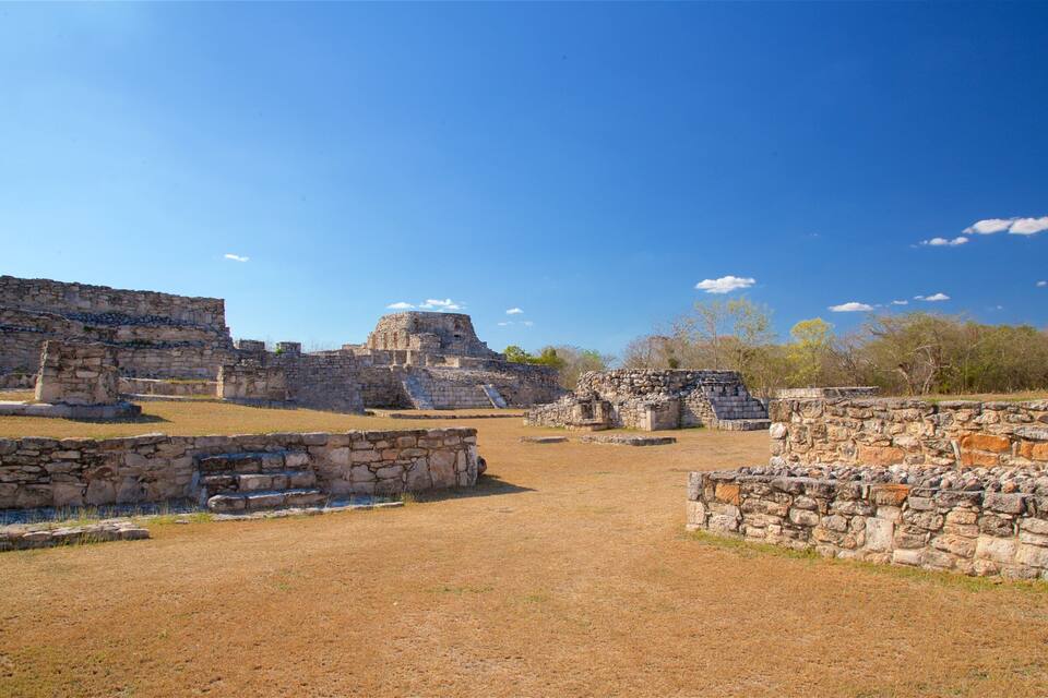 Antiguas ruinas de piedra con pirámides escalonadas y estructuras de techo plano bajo un cielo azul despejado.