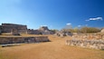 Ancient stone ruins with stepped pyramids and flat-topped structures under a clear blue sky.