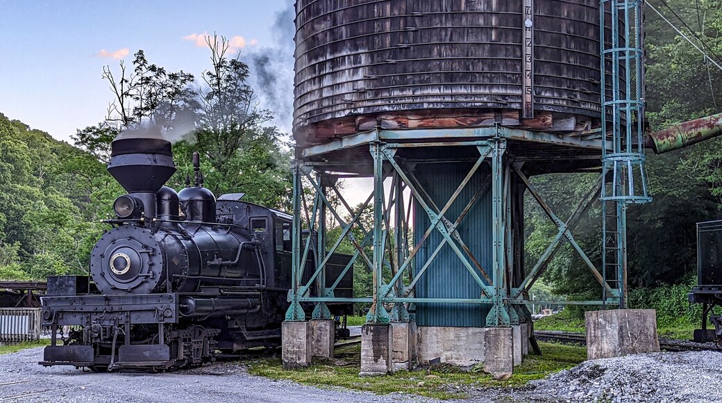 View of an Antique Shay Steam Engine Warming Up by an Old Water Tower Blowing Smoke