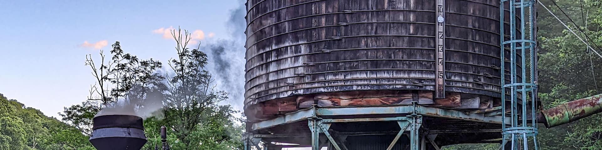 View of an Antique Shay Steam Engine Warming Up by an Old Water Tower Blowing Smoke