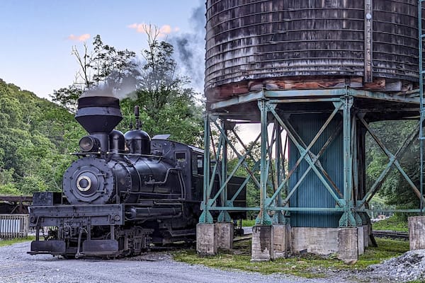 View of an Antique Shay Steam Engine Warming Up by an Old Water Tower Blowing Smoke