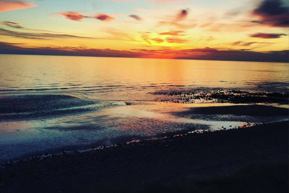 Een zonsondergang boven een rustige zee met een rotsachtige kustlijn.