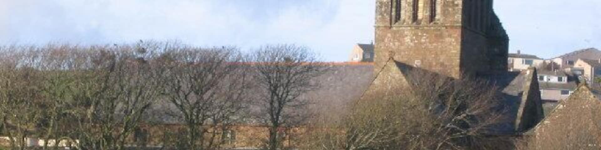 A historic tower with arched windows, surrounded by trees and a fenced field.