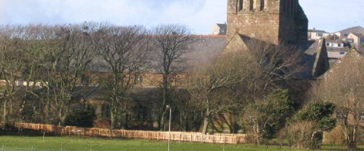 A historic tower with arched windows, surrounded by trees and a fenced field.