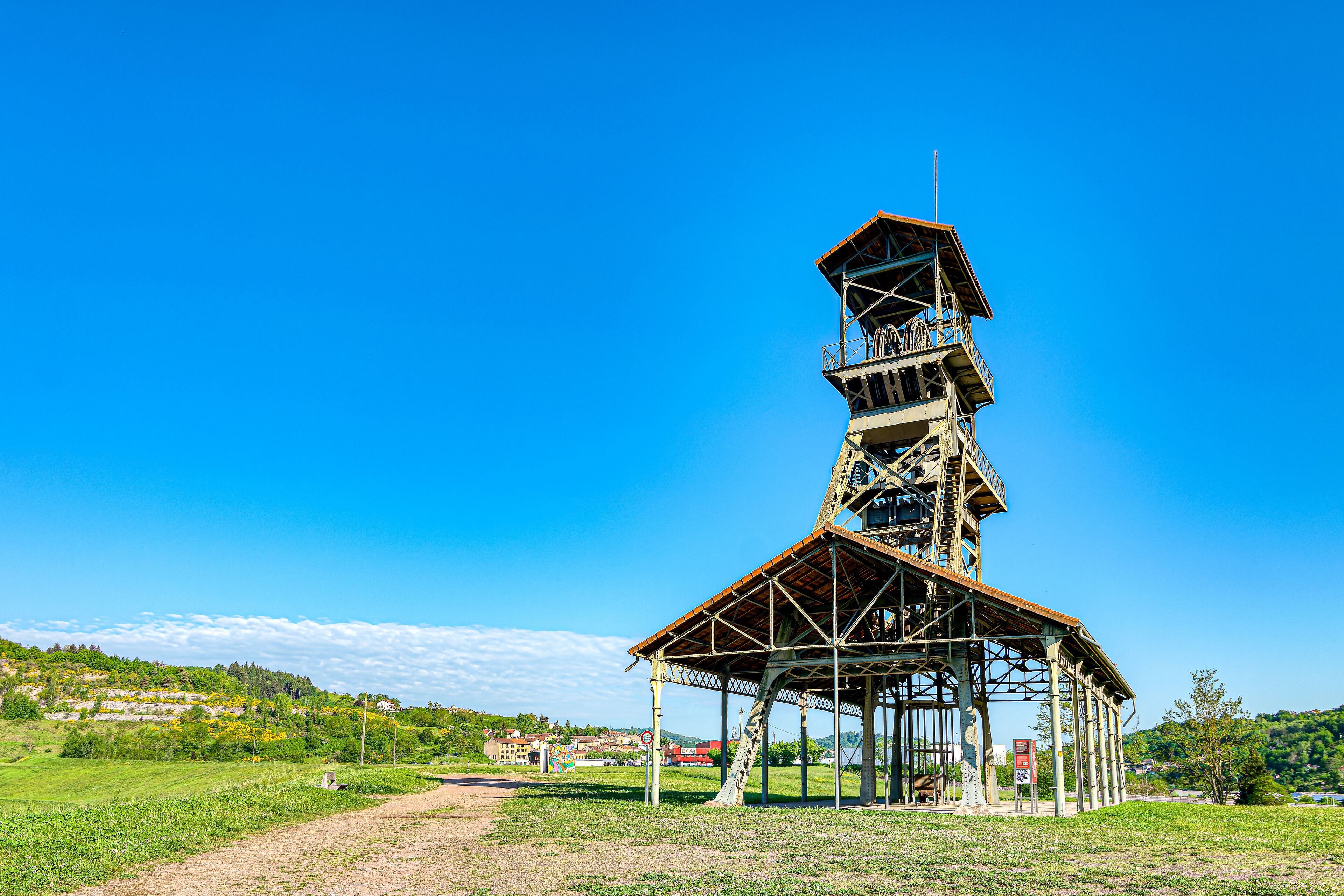 A metal tower with a wooden platform, surrounded by a grassy field and a clear blue sky.