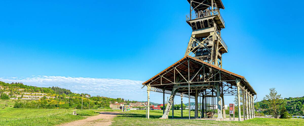 A metal tower with a wooden platform, surrounded by a grassy field and a clear blue sky.