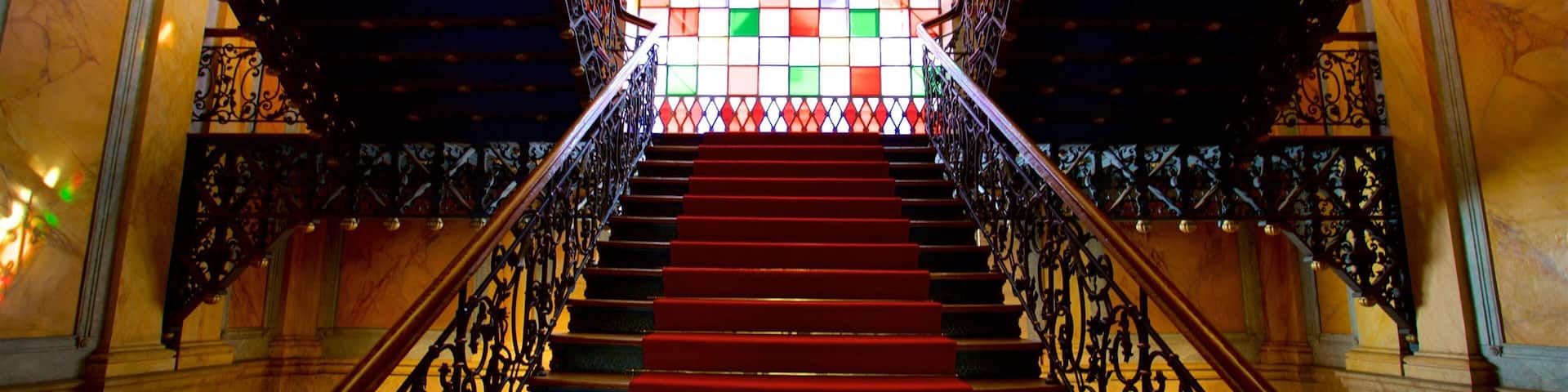 A grand staircase with ornate metal railings and a colorful stained glass window at the top.