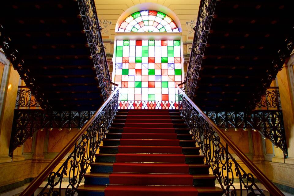 Una àmplia escala amb barana metàl·lica ornamentada i una finestra de vitralls de colors a la part superior.
