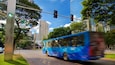 Un autobus bleu dans une rue de la ville, avec des feux de signalisation et un panneau indiquant « Praça Diogo de Vasconcelos ».