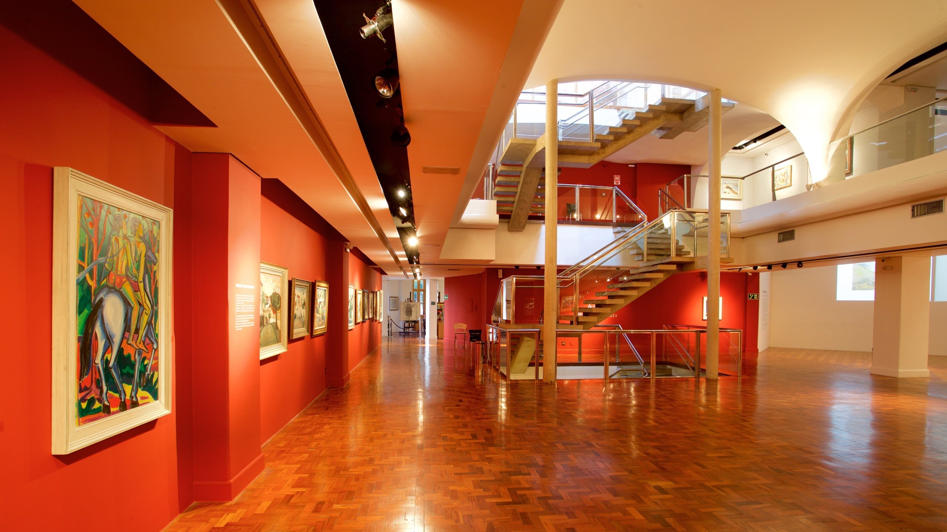 An art gallery with red walls, wooden floors, and a staircase.