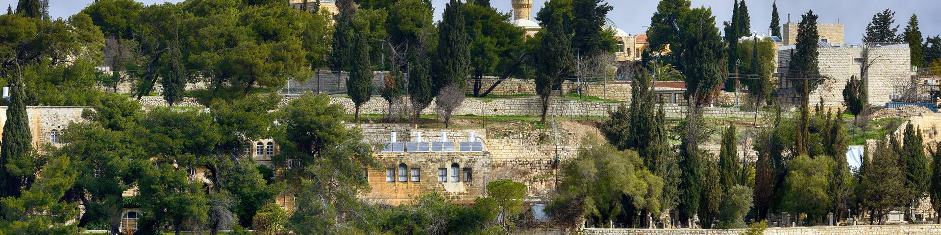 A historic church with a dome and bell tower, surrounded by lush greenery and ancient stone walls.