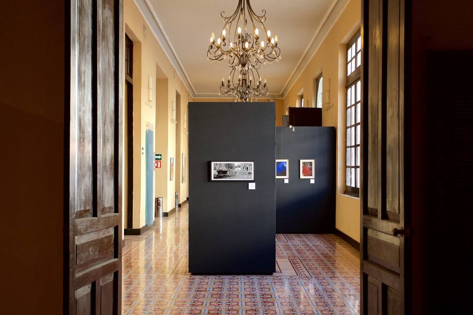 A hallway with a patterned floor, a chandelier, and framed pictures on the walls.