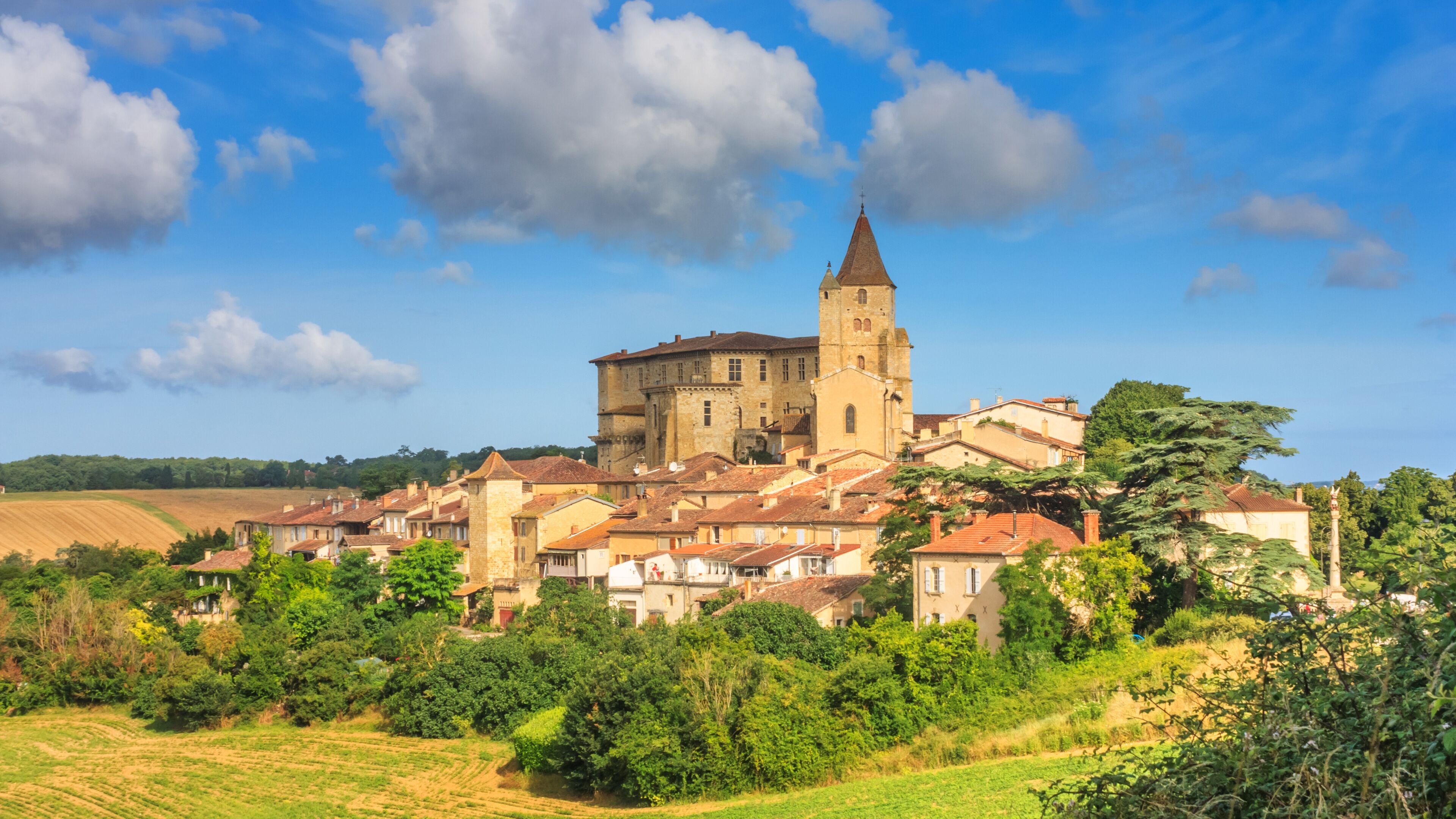A historic town with a prominent church tower, surrounded by lush greenery and terraced fields.