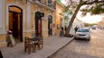 A street with a restaurant, outdoor seating, and parked cars.