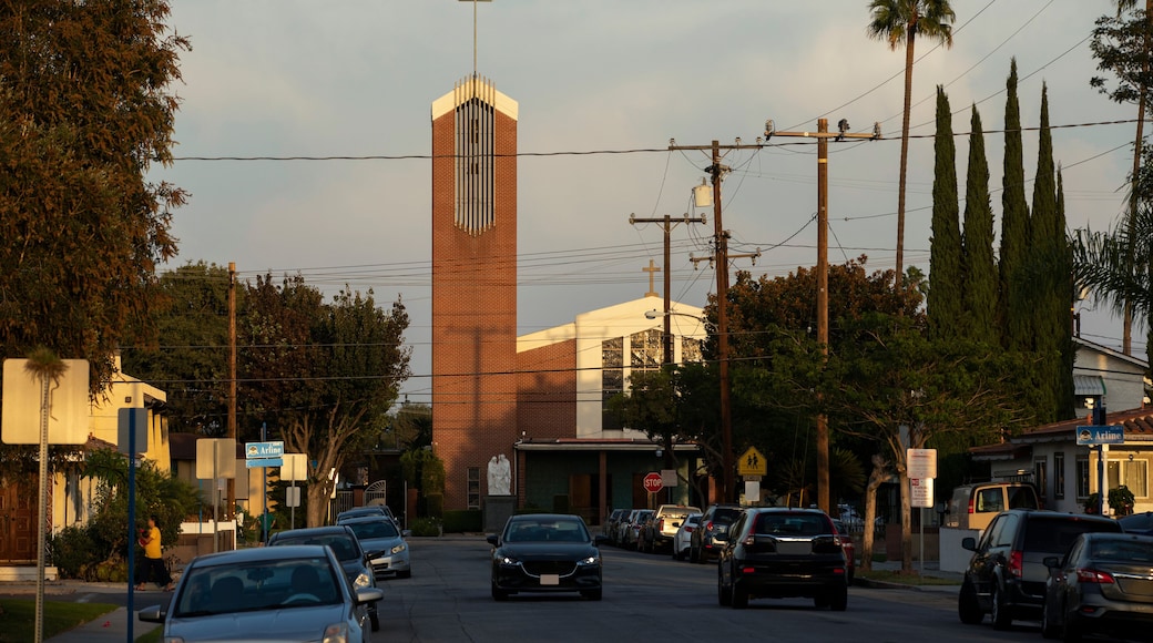 Une rue bordée de voitures, une église surmontée d’une croix et des palmiers.