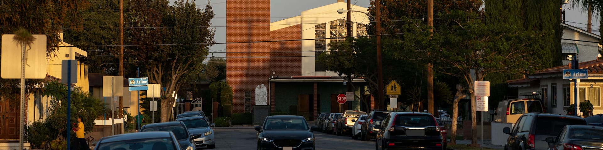 A street with cars, a church with a cross, and palm trees.