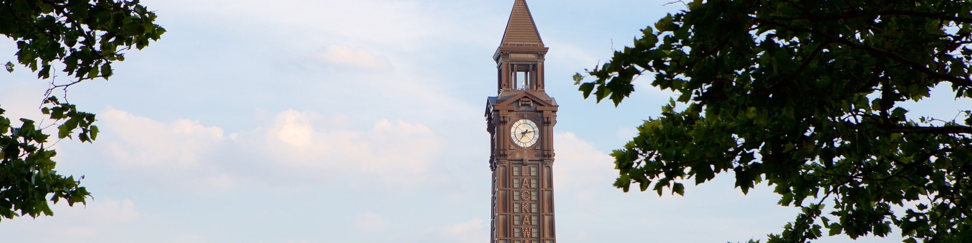 Ein Uhrturm mit spitzem Dach, umgeben von Gebäuden mit begrünten Dächern und aufwendiger Architektur.