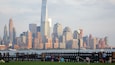 En stadsbild med en framträdande skyskrapa, en hamnfront och människor som sitter på en gräsyta.