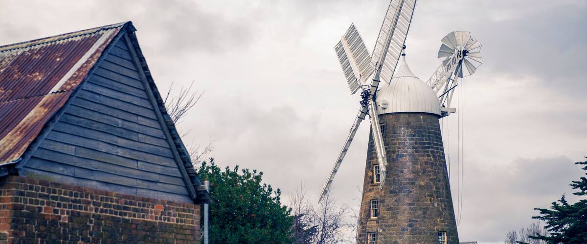 A windmill with two sails, a brick building, and a cloudy sky.