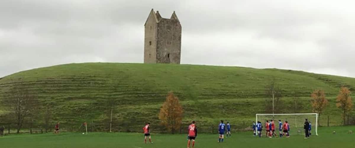 A grassy field with a castle on a hill and a soccer game in progress.
