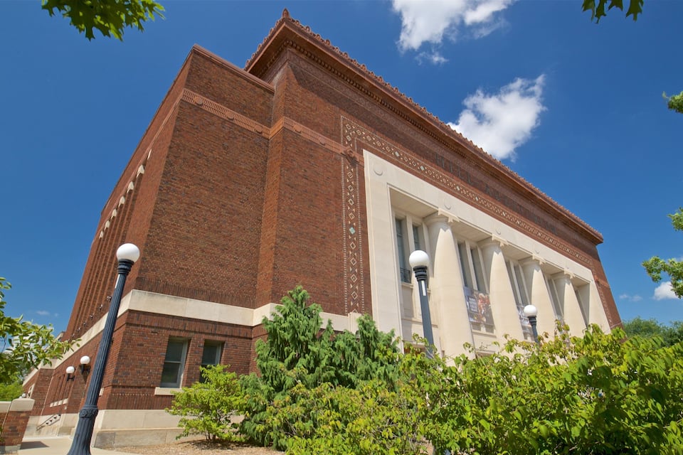 A large brick building with a central entrance and columns, surrounded by greenery.