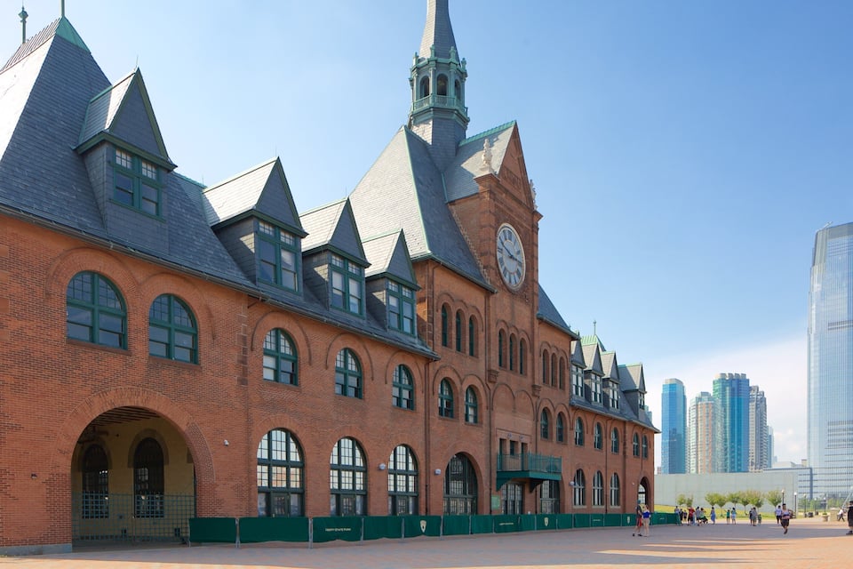 A historic brick building with a clock tower and pointed roofs, surrounded by modern skyscrapers.