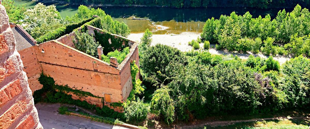A historic brick structure with a river and dense greenery in the background.