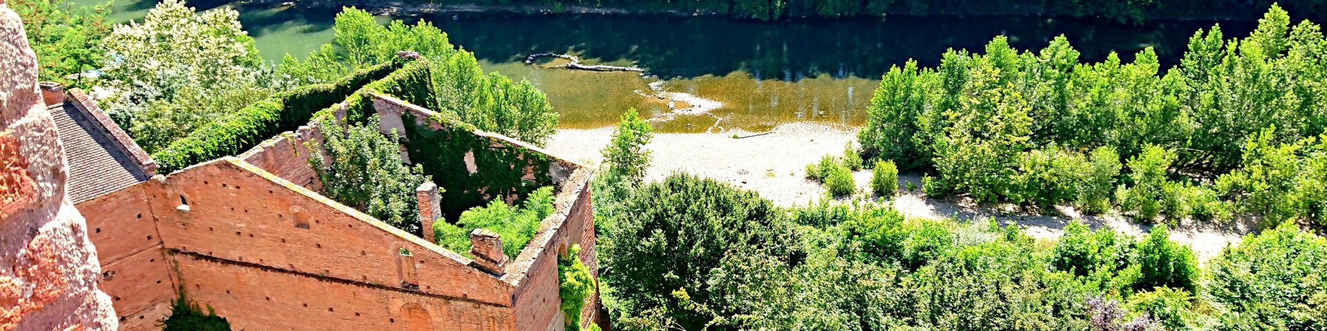 A historic brick structure with a river and dense greenery in the background.