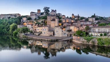 A historic town with stone buildings, a castle, and a calm river reflecting the architecture.