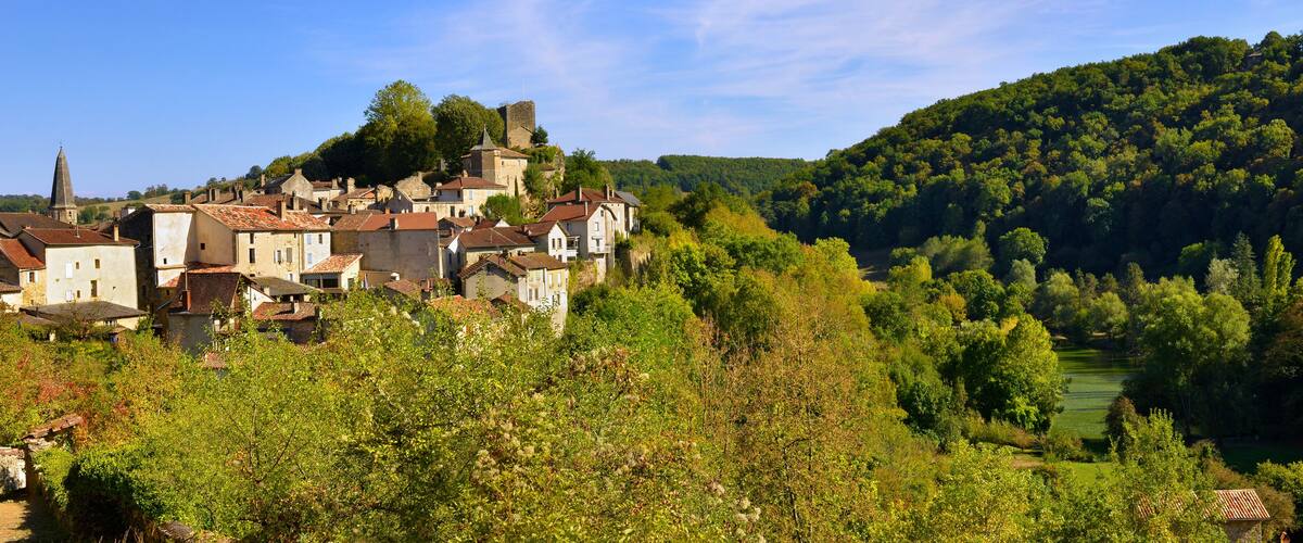 A historic town nestled in a valley with a prominent church tower, surrounded by lush greenery and a river.