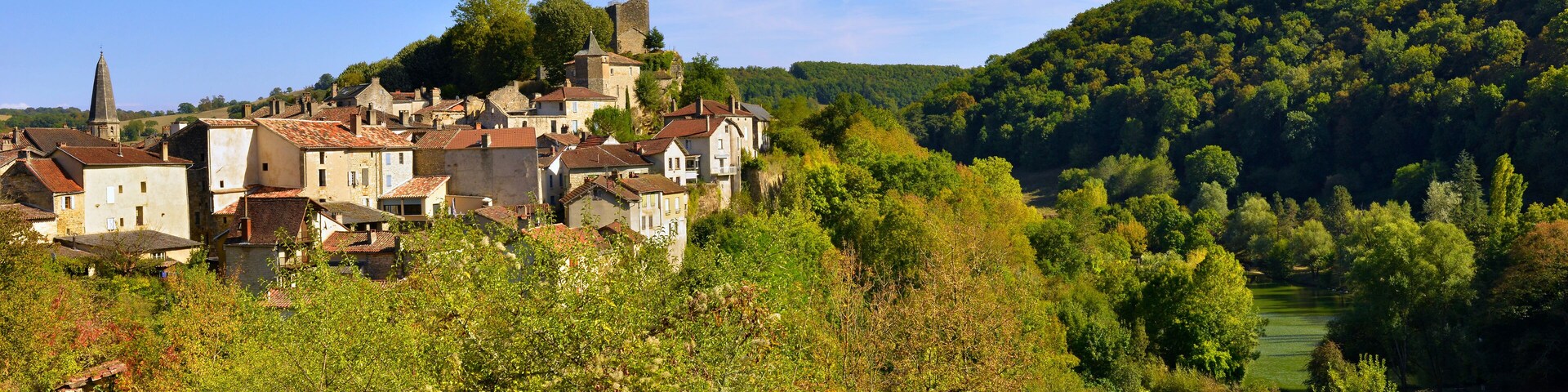 A historic town nestled in a valley with a prominent church tower, surrounded by lush greenery and a river.