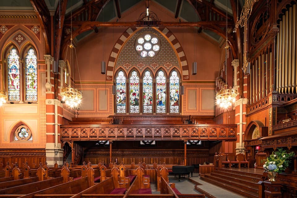 An ornate church interior with stained glass windows, wooden pews, and a pipe organ.