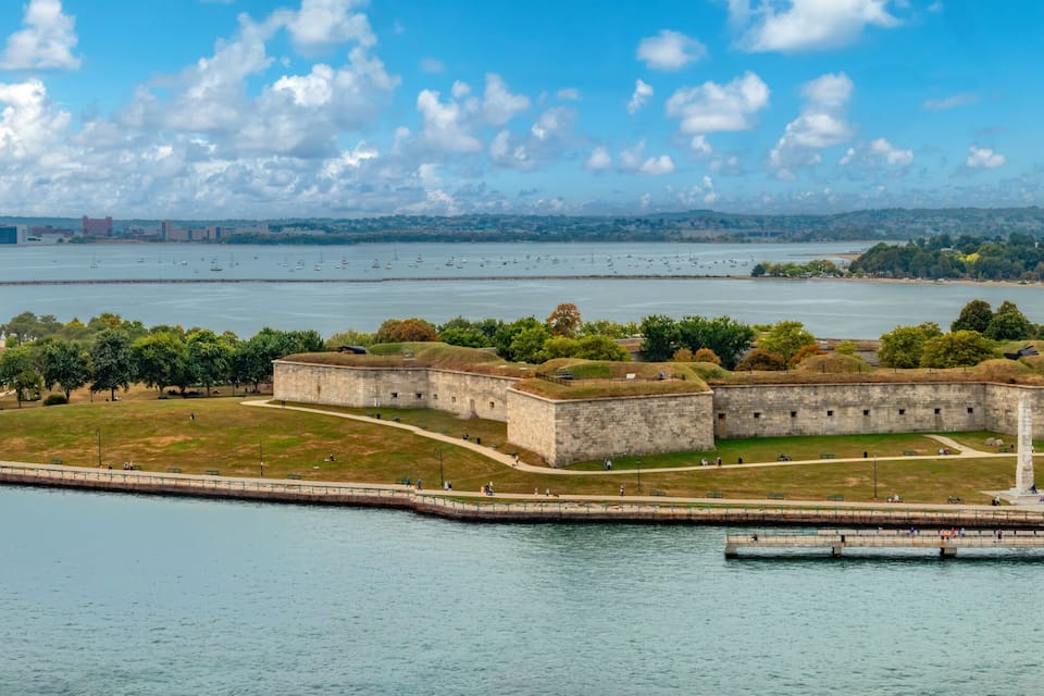 A coastal fortification with a lighthouse, surrounded by water and greenery.