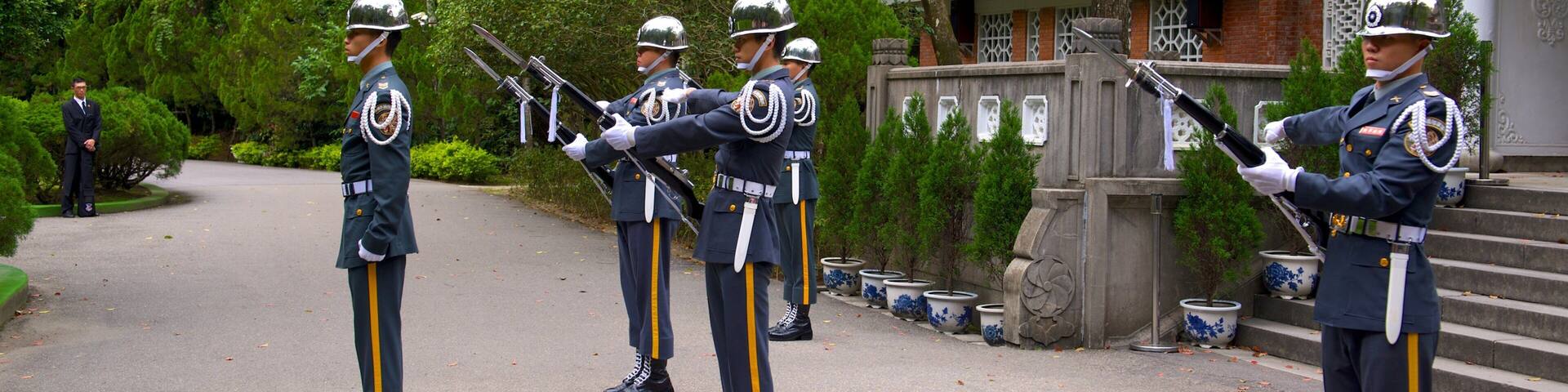 A group of uniformed guards in ceremonial attire standing in formation on a paved path.