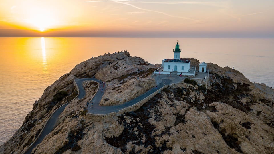A coastal landscape with a lighthouse on a rocky outcrop, a winding road, and the ocean in the background.
