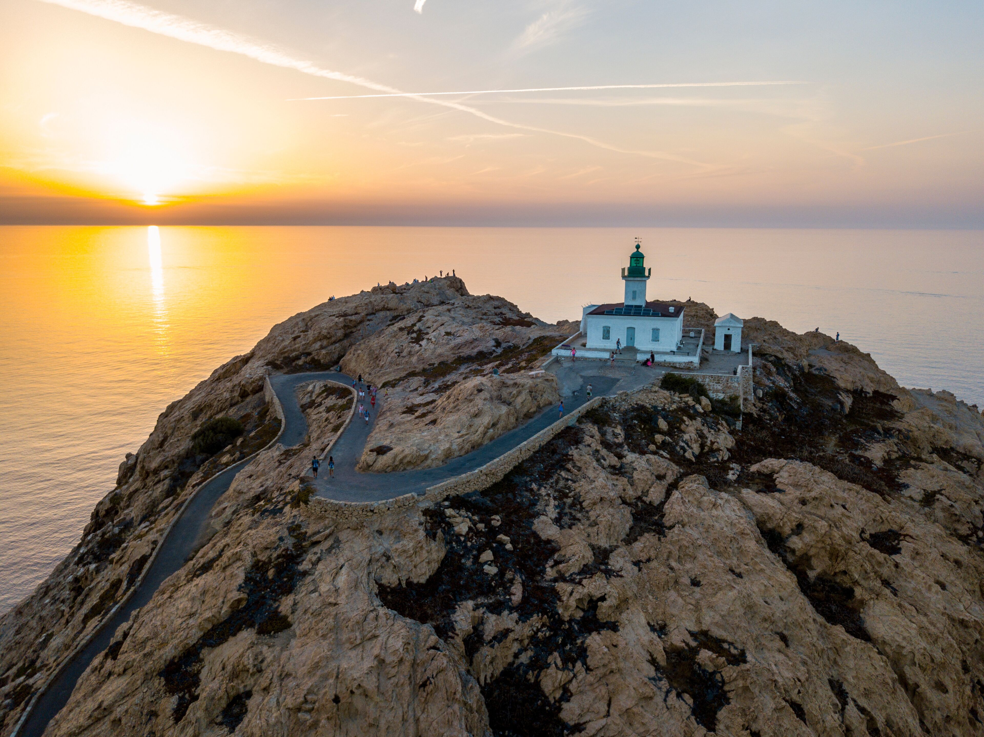 A coastal landscape with a lighthouse on a rocky outcrop, a winding road, and the ocean in the background.