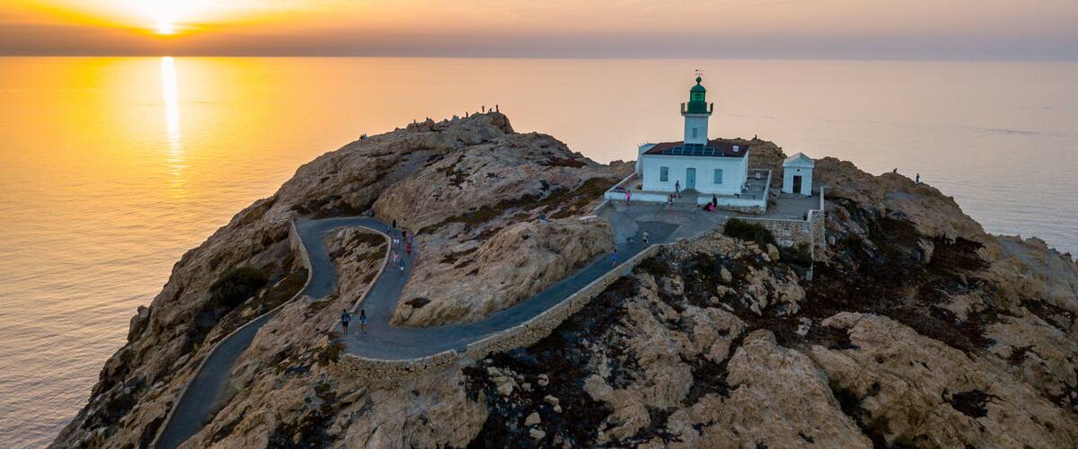 A coastal landscape with a lighthouse on a rocky outcrop, a winding road, and the ocean in the background.