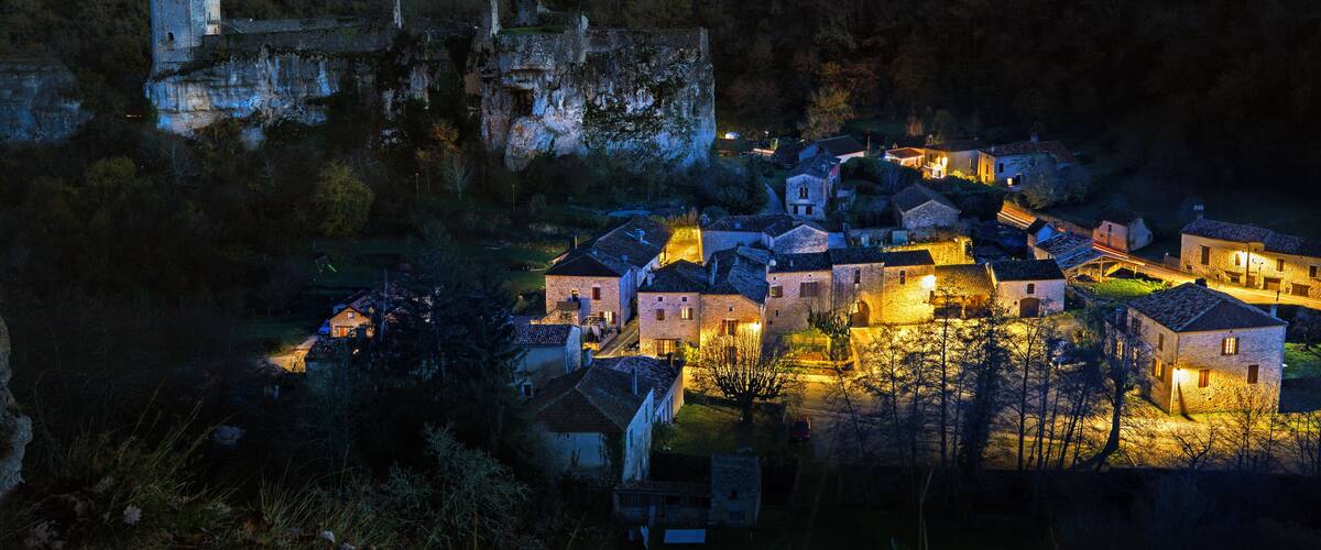 A historic village at dusk with illuminated buildings and a prominent castle on a hill.