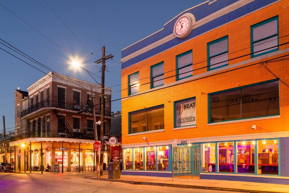 A brightly lit street corner at dusk with a vintage building featuring a clock and a storefront with a sign for 'Beat Magazine'.