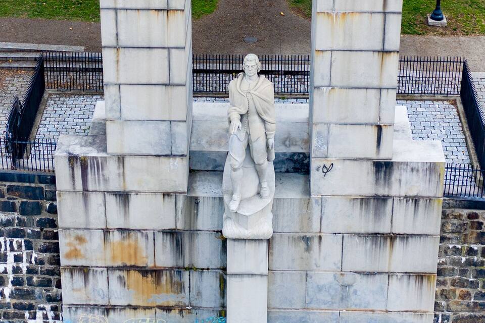 Monument antic i desgastat amb grafitis, envoltat per una paret de maó i una tanca metàl·lica.