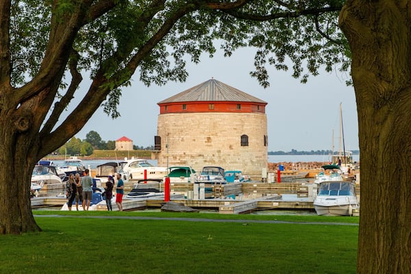 Une tour historique surmontée d’un toit rouge, entourée de bateaux et d’arbres, dans un cadre de port de plaisance.