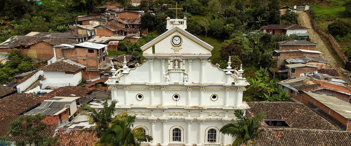 A white church with a clock, surrounded by residential buildings and palm trees.