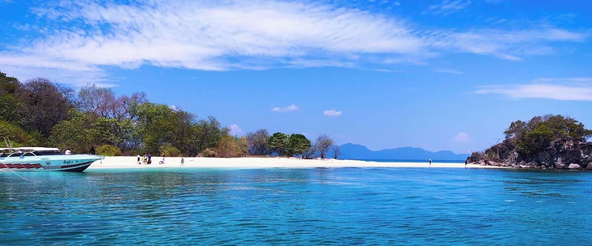 A clear turquoise sea with a boat named "FARIS 2" anchored near a sandy beach with people and trees.