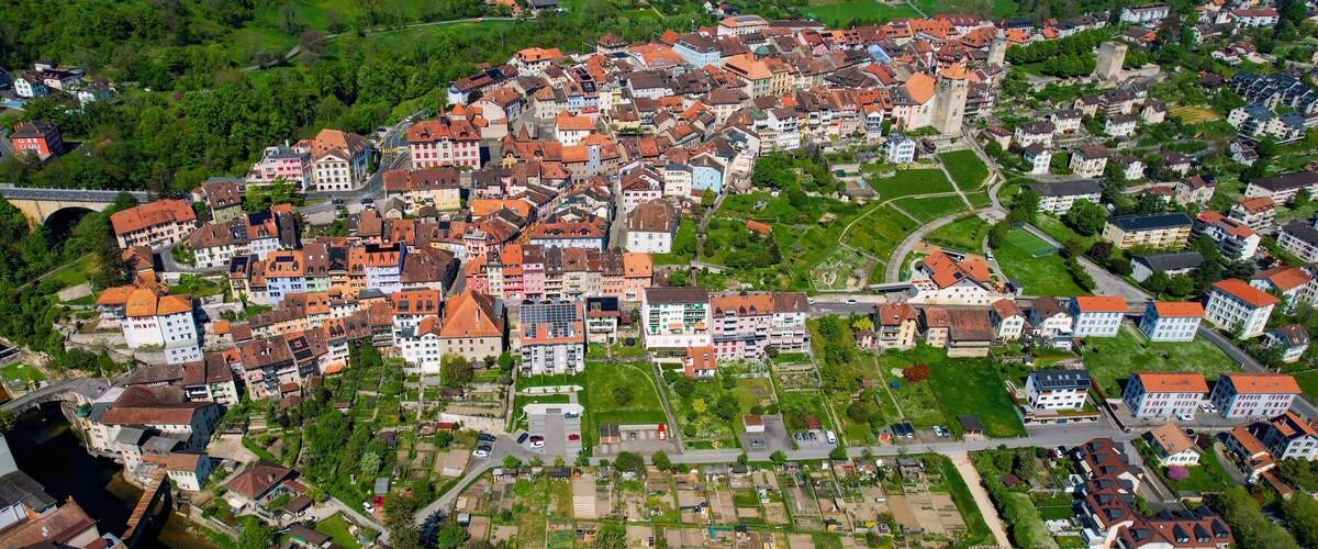 An aerial view of a town with a river, green fields, and a mix of traditional and modern buildings.